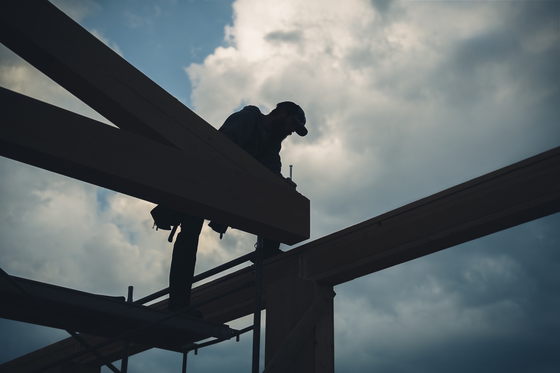 Worker on timber frame structure against cloudy sky
